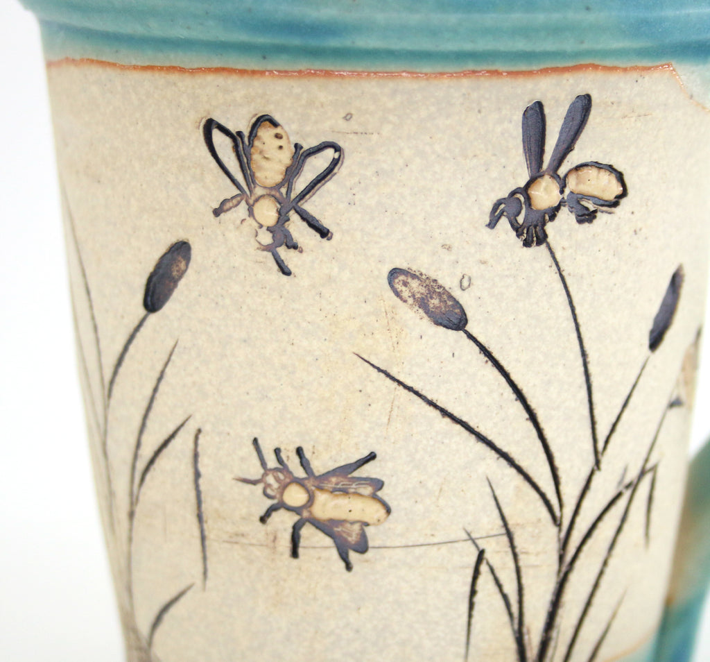 Coastal themed pottery, high fired stoneware mug with a hand etched design of bees flying over cattails. Close up detail.