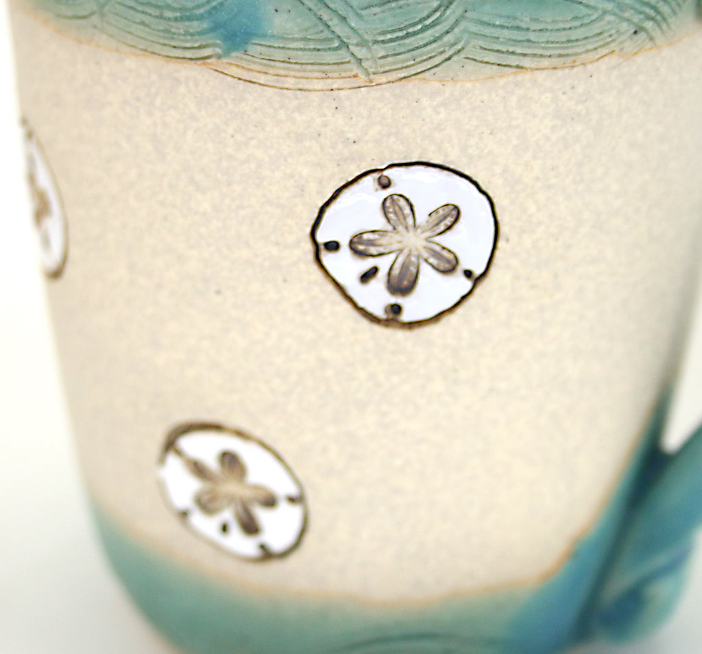 Coastal themed stoneware mug in Caribbean Blue with hand carved sand dollar design. Close up detail.